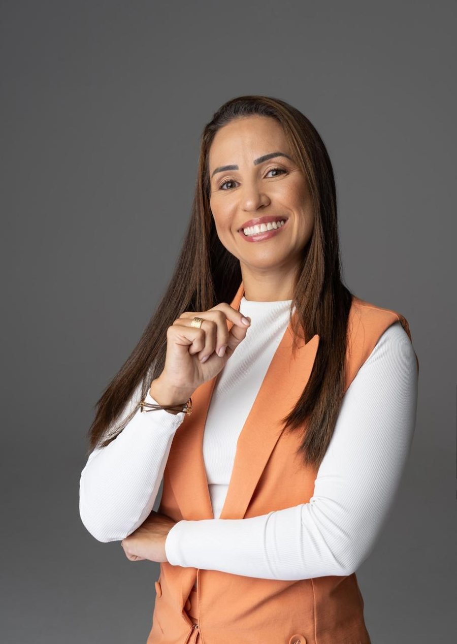 Dra. Priscilla Aquino sorrindo, de colete cor terracota, em retrato profissional
