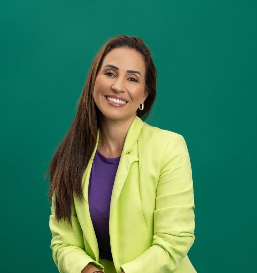 Dra. Priscilla Aquino sorrindo, de blazer verde-lima sobre fundo verde